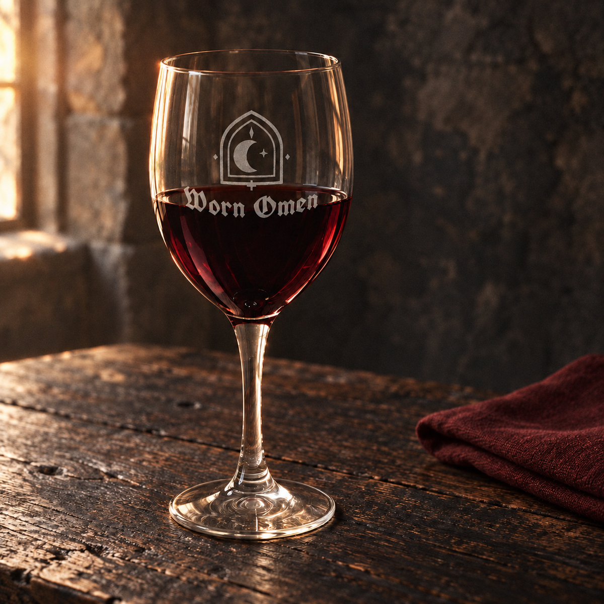 WORN OMEN VESPER wine glass with red wine on an old oak table and oxblood linen.