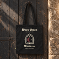 WORN OMEN WANDERER black canvas tote hanging against a weathered timber door.