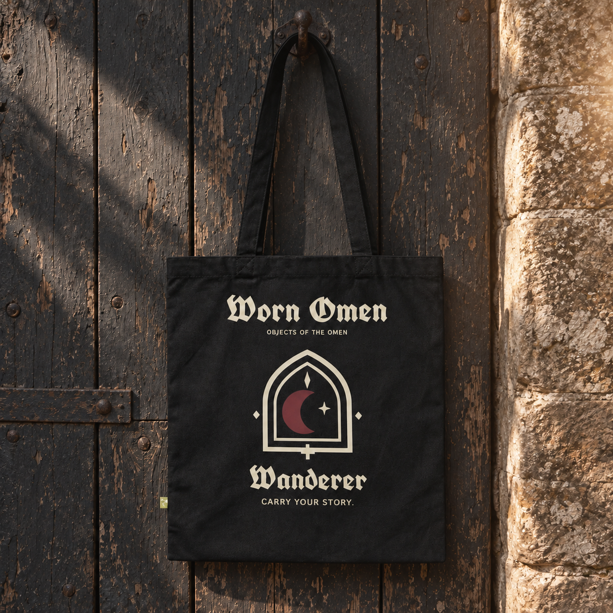WORN OMEN WANDERER black canvas tote hanging against a weathered timber door.