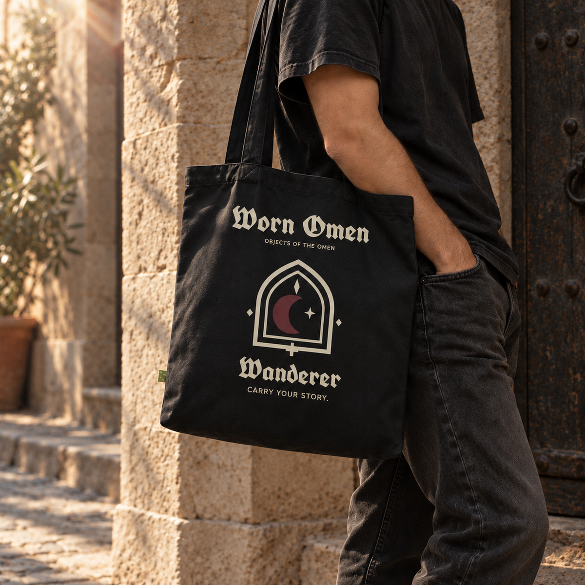 WANDERER organic canvas tote carried at the hip in a stone courtyard.
