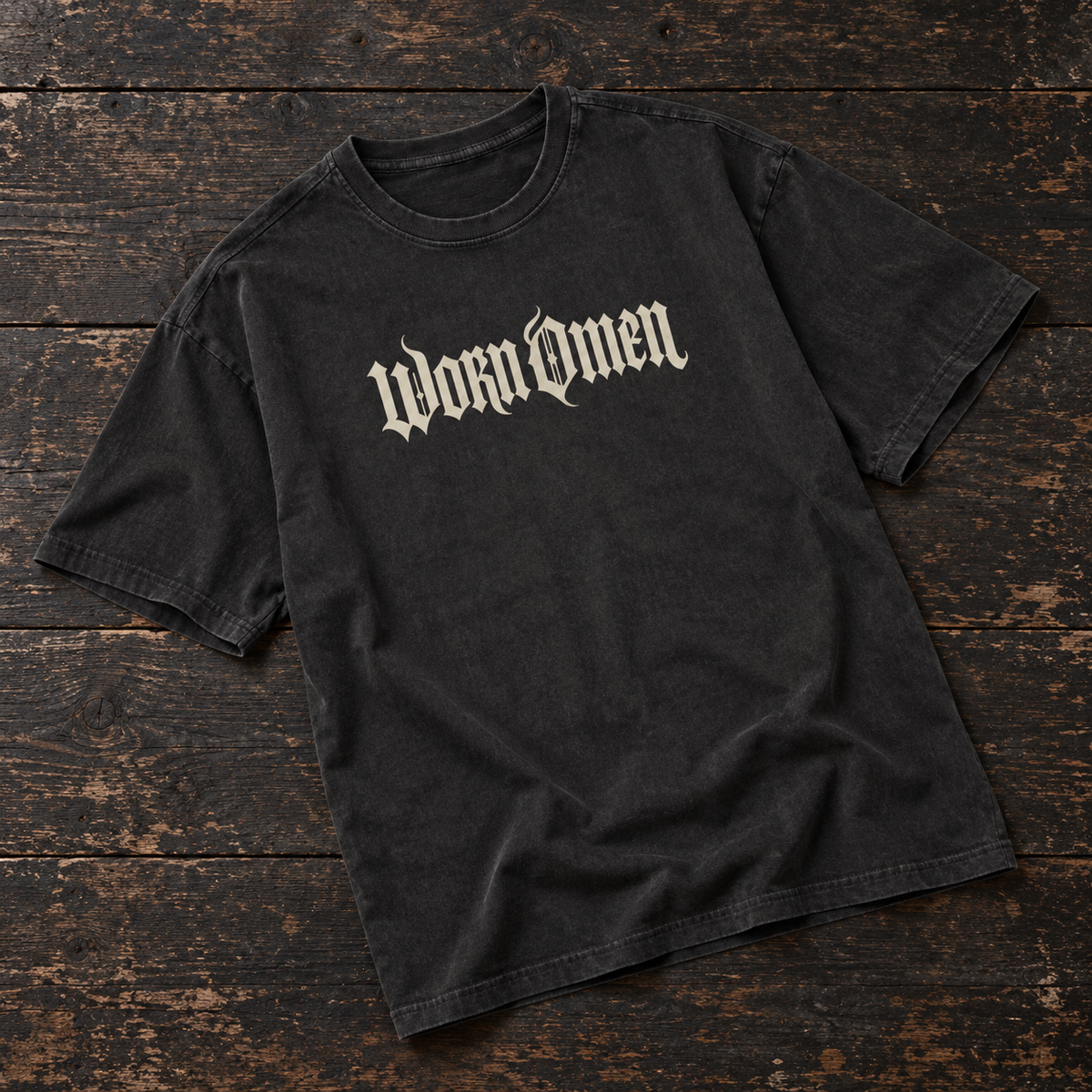 WORN OMEN oversized gothic T-shirt in acid-washed black with bone lettering, laid on dark timber
