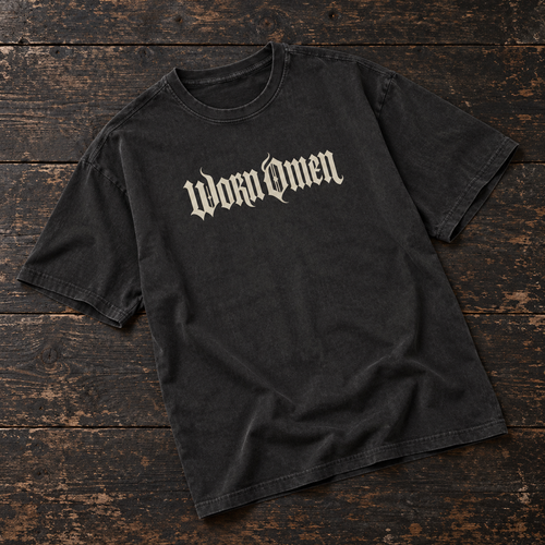 WORN OMEN oversized gothic T-shirt in acid-washed black with bone lettering, laid on dark timber