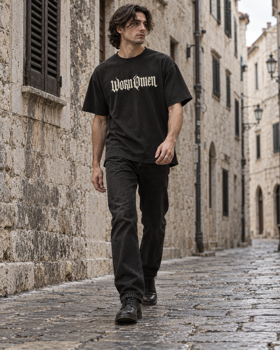 Model walking along a stone street in the WORN OMEN oversized gothic T-shirt