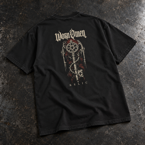 WORN OMEN Relic solid-black oversized tee with ornate key artwork on the back, laid on weathered steel